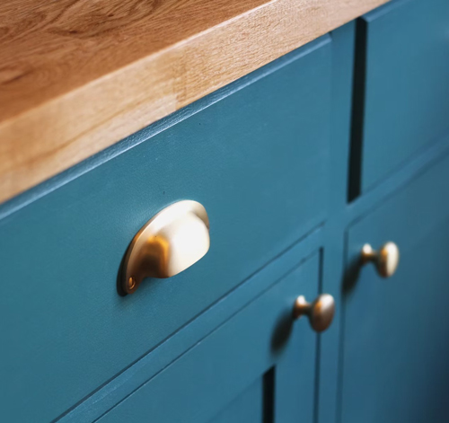 close up of kitchen cabinet featuring teal paint with a wooden countertop and brass handles highlighting modern design and functionality