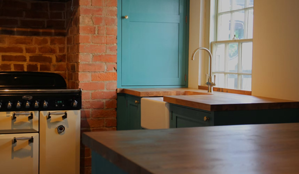 a modern kitchen with teal cabinetry wooden countertop exposed brick wall and a black stove featuring a kitchen sink and a bright window incorporating contemporary design for four cooking essentials